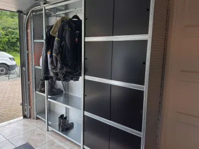 Metalen stellingkast in garage met motorhelmen, motorjassen en laarzen voor georganiseerde opslag.