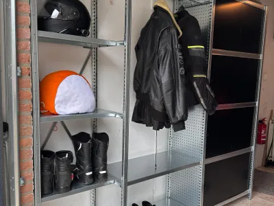 Garageopslag met metalen stellingkast, hangruimte voor motorjassen en planken voor overige materialen.