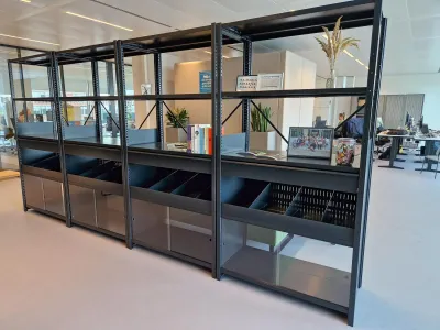 Zwart gecoate stellingkast met schuifdeurtjes en vakverdeelsets midden in een kantoorruimte voor visuele scheiding.