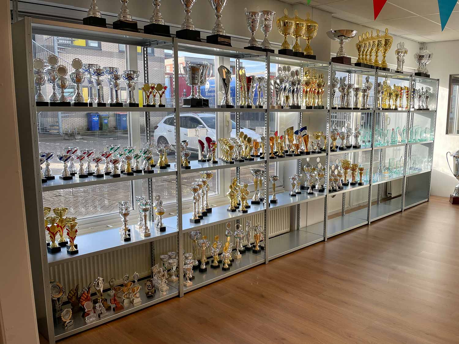 Stellingkasten gevuld met sportbekers en trofeeën in de winkel van Eurosportprijzen.