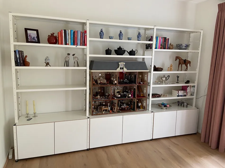 Witte stellingkast in woonkamer met onderdeuren en open planken.