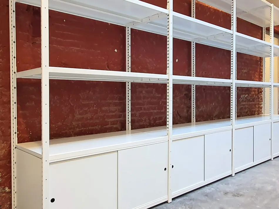 Witte stellingkast tegen stenen muur met witte schuifdeursets.